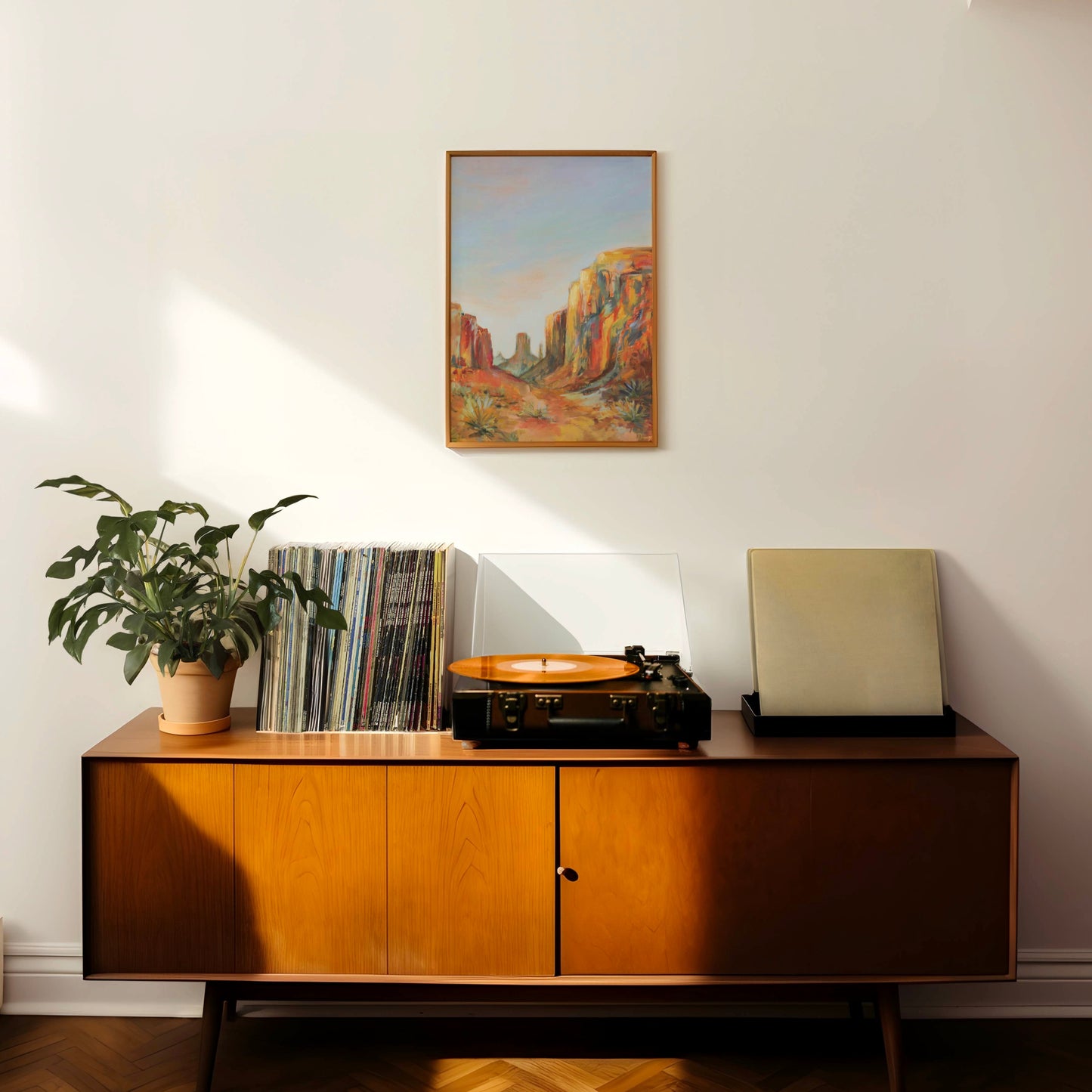 Wooden sideboard with vinyl records and a plant in a room with an Arizona southwestern desert painting on the wall.