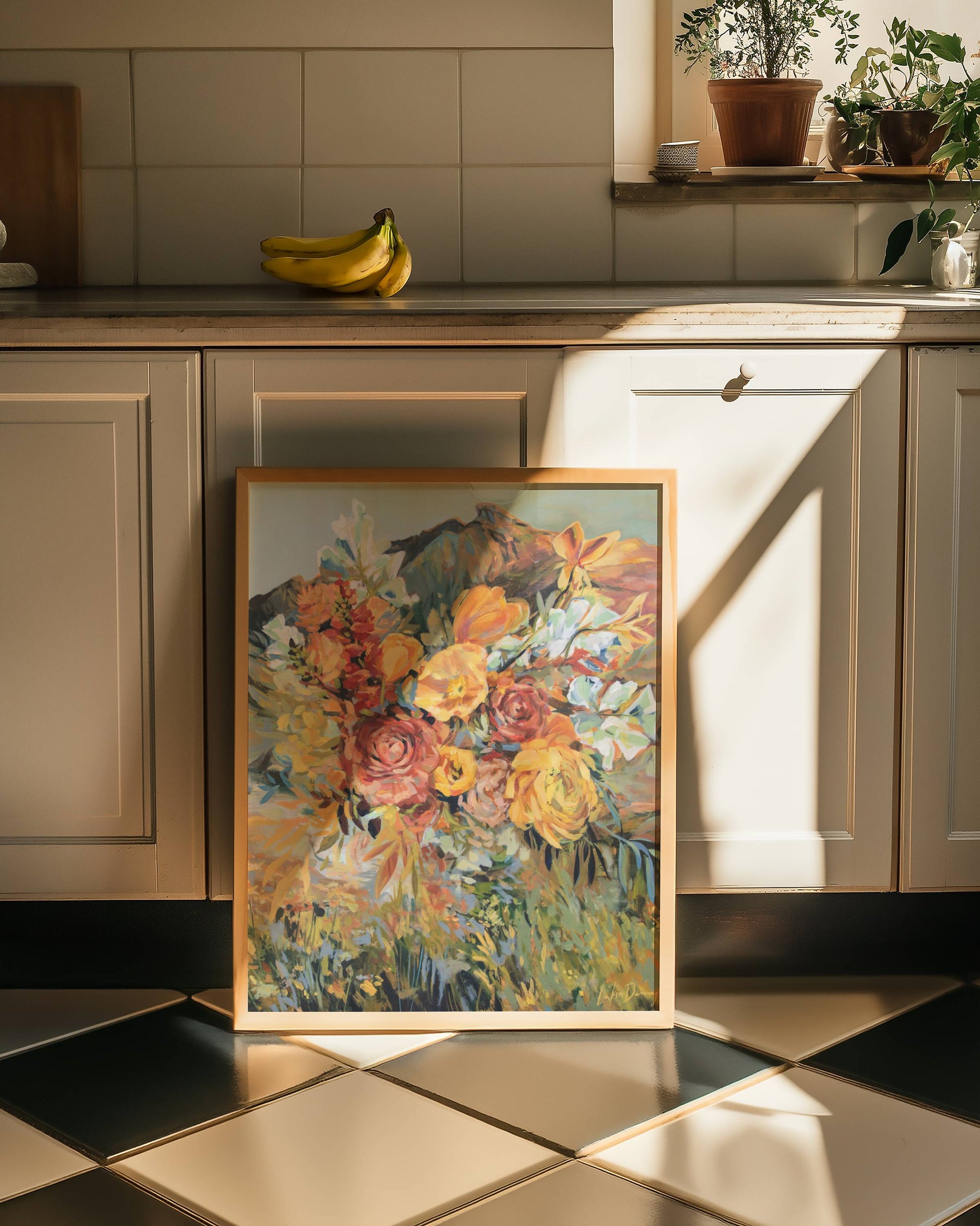 Framed floral painting on a kitchen counter with cabinets and plants in the background