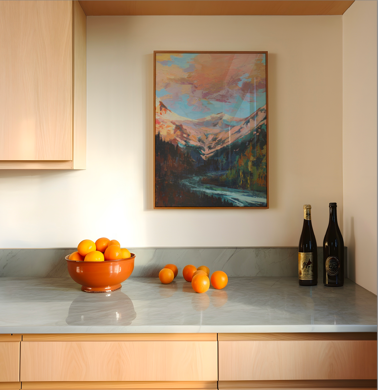 Kitchen counter with a bowl of oranges, scattered oranges, and wine bottles, with a mountain painting on the wall.