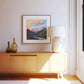 Modern interior with wooden cabinet, lamp, and framed mountain landscape painting.